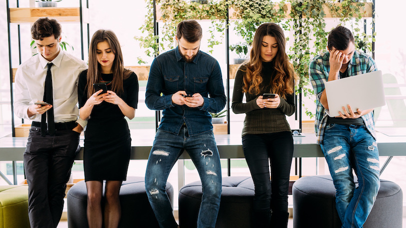 5 young professionals standing together staring at their phones