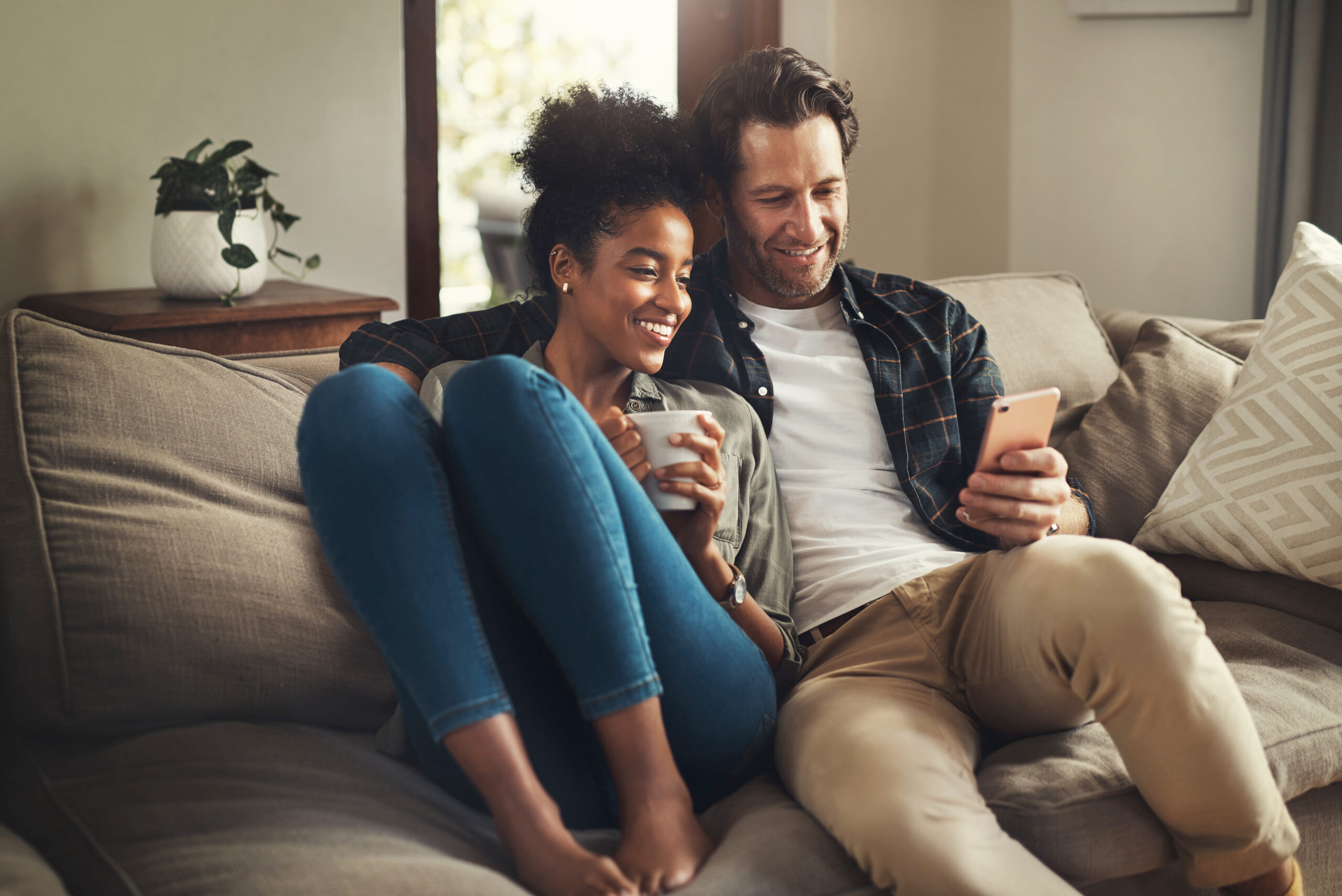 Young couple sitting on couch and looking at digital tablet, smiling.