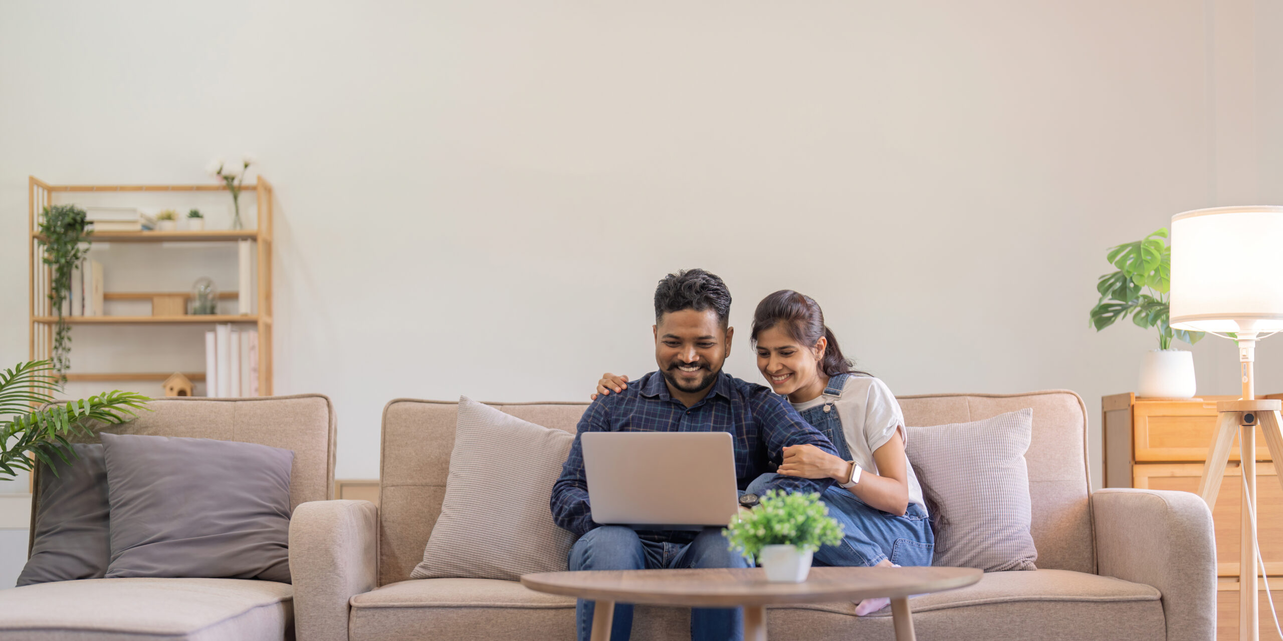 man and woman sitting on couch looking at open laptop and smiling
